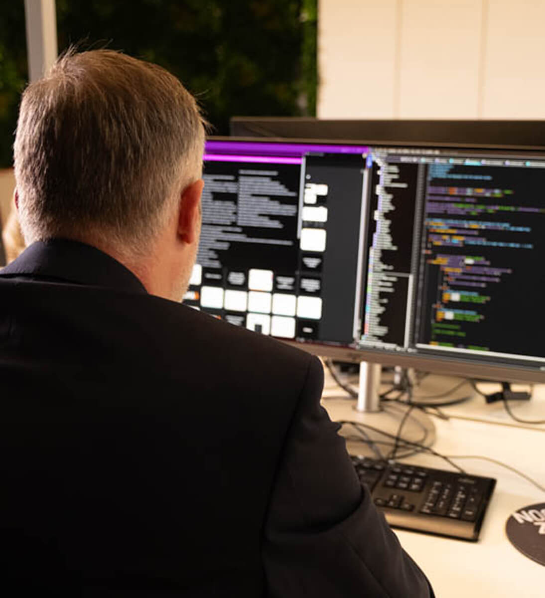 A business man is shown from the back in front of a big screen with code. Symbol image for AI solutions.
